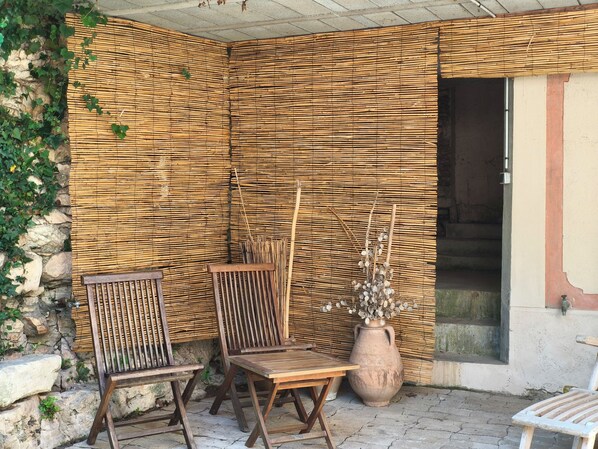 Un espace extérieur abrité, aménagé avec du mobilier en bois et un grand pot en terre cuite.