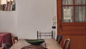 Un área de comedor con una mesa de madera, sillas, una lámpara colgante negra, una estantería y una puerta con ventanal.