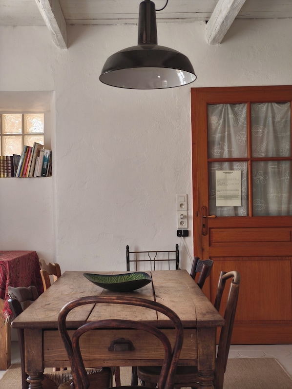 Een eetgedeelte met een houten tafel, stoelen, een zwart hanglamp, een boekenkast en een deur met een raam.