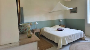 Un dormitorio con cama, mesitas de noche, lámpara colgante, un jarrón y un cuadro en la pared.