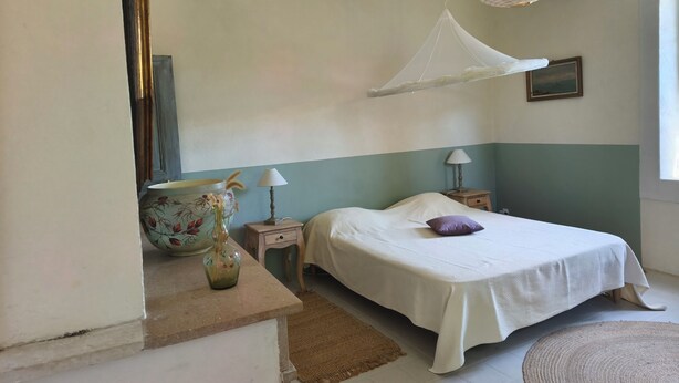 Une chambre à coucher avec un lit, des tables de chevet, un luminaire suspendu, un vase et un tableau au mur.