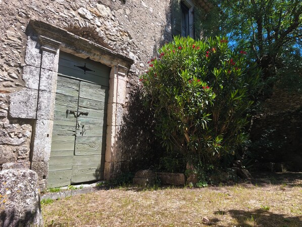 A stone building with a green door, a small garden with red flowers, and a tree. - Quiet village farmhouse with a terrace and garden, (Goudargues)