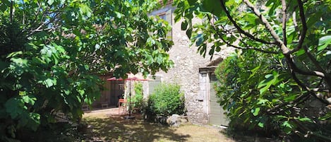 Un edificio de piedra con techo rojo, rodeado de abundante vegetación y un área verde.
