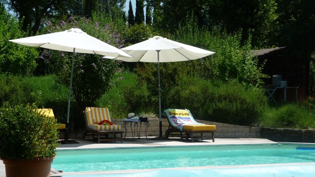 A pool area with two lounge chairs and two umbrellas, surrounded by greenery. - Furnished T2 (3 stars) with terrace and pool in the Luberon Côté Sud. (La Tour-D'aigues)