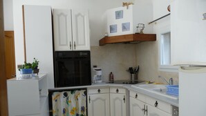 A compact kitchen with white cabinets, a black oven, a coffee maker, and a small potted plant. - Furnished T2 (3 stars) with terrace and pool in the Luberon Côté Sud. (La Tour-D'aigues)