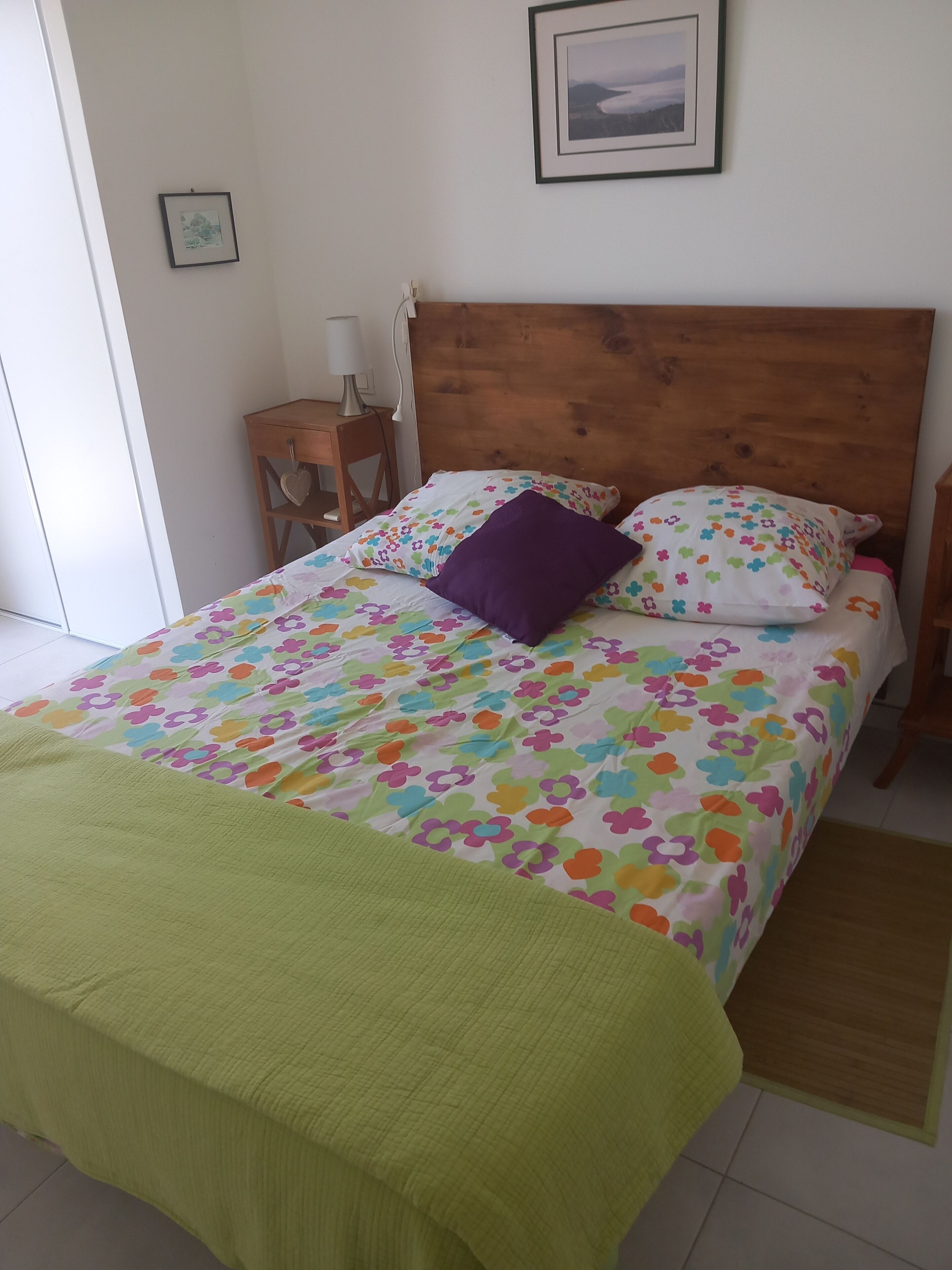 A bed with a floral bedspread, a wooden headboard, and a green throw blanket.