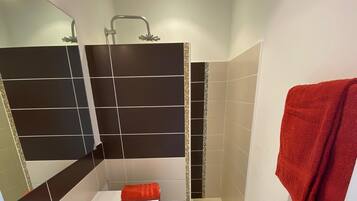Een moderne badkamer met een witte wastafel, zwart en beige tegels, een rode handdoek en een douchehoek.