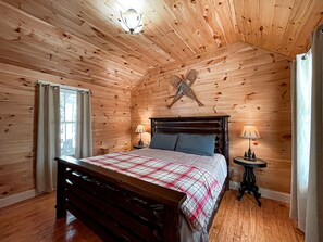 Une chambre à coucher aux murs lambrissés, avec un lit, deux lampes de chevet, une petite table et une étoile décorative accrochée au mur.