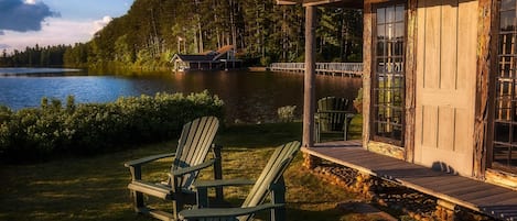 A lakeside cabin with a dock, two Adirondack chairs, and a wooden deck.