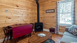 A cozy cabin interior with a wooden interior, a fireplace, a dining table, and a sofa.