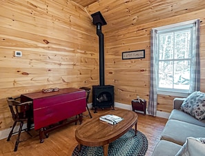 A cozy cabin interior with a wooden interior, a fireplace, a dining table, and a sofa. - Longfellow a Traditional Cabin (Paul Smiths)