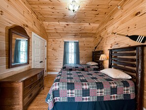 A wooden cabin bedroom with two beds, a dresser, a mirror, and a lamp. - Longfellow a Traditional Cabin (Paul Smiths)