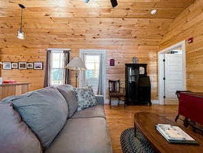 A cozy living room with a wooden ceiling, a sofa, a lamp, and a red table. - Longfellow a Traditional Cabin (Paul Smiths)