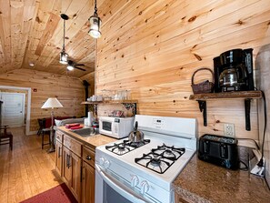 Une cuisine de taille réduite avec des murs en bois, une cuisinière à gaz, un four à micro-ondes et une machine à café.