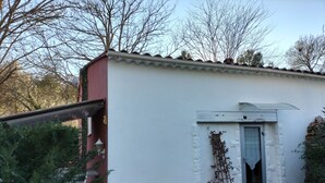 A small, single-story building with a white exterior, a red door, and a small window. - lodging the rosemary: implanted in a green frame under the sun of midday. (Le Thoronet)