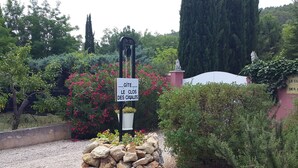 A sign reading "Gîte Le Clos Des Cigares" in a garden setting with a stone wall, potted plants, and a variety of trees. - lodging the rosemary: implanted in a green frame under the sun of midday. (Le Thoronet)