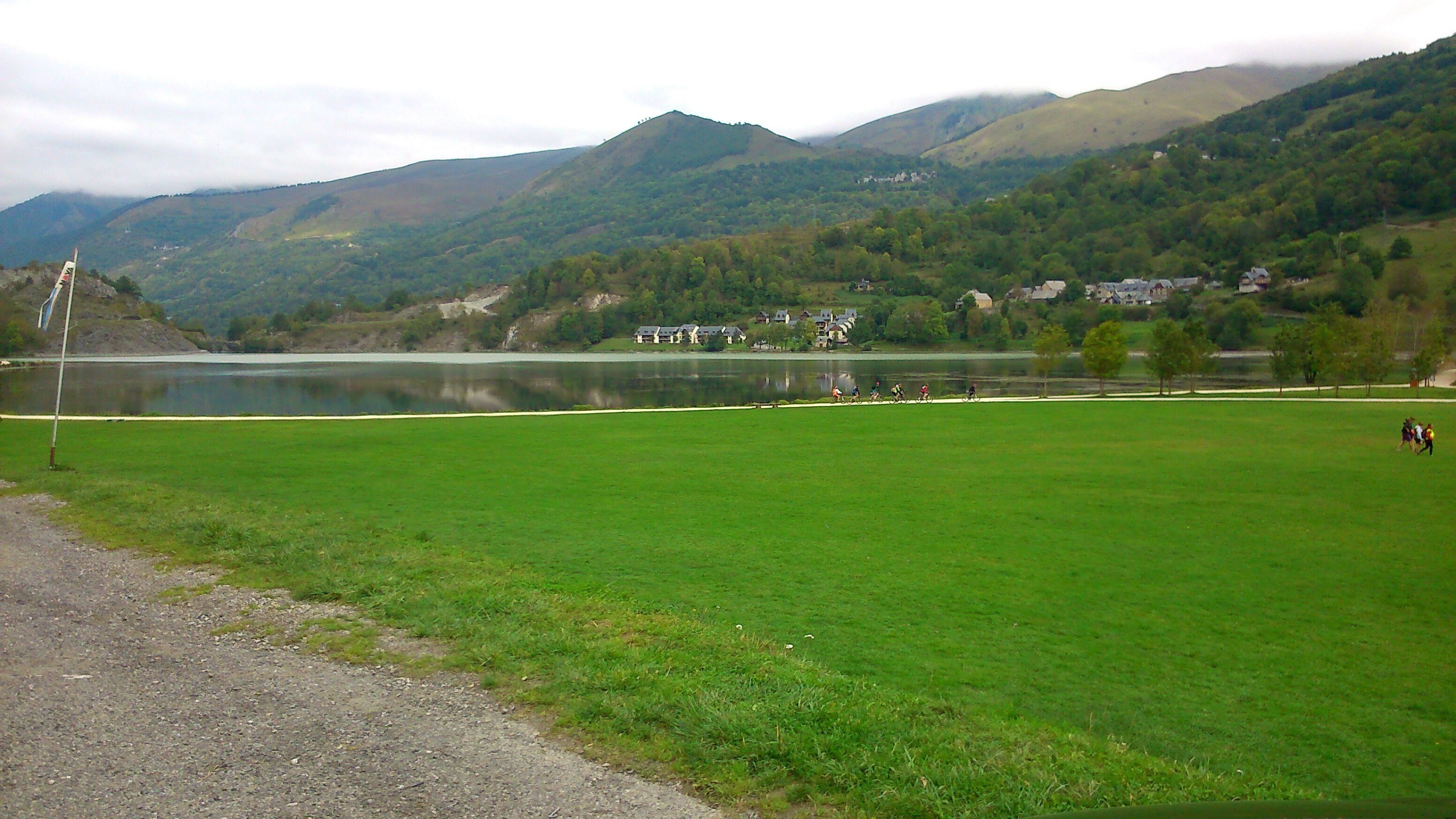 A lakeside view with a grassy area, a small building, and mountains in the background.