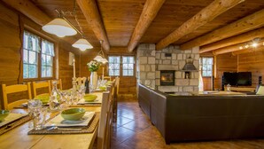 A wooden cabin interior with a dining area, stone fireplace, and a TV.