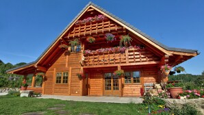 A wooden log cabin with a sloped roof, large windows, and flower boxes on the porch.