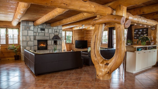 A rustic cabin interior with a stone fireplace, wooden beams, a stone wall, a wooden bench, a television, and a wooden cabinet.