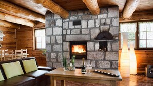 A cozy room with a stone fireplace, wooden beams, a sofa, and a table with a bottle and glasses.