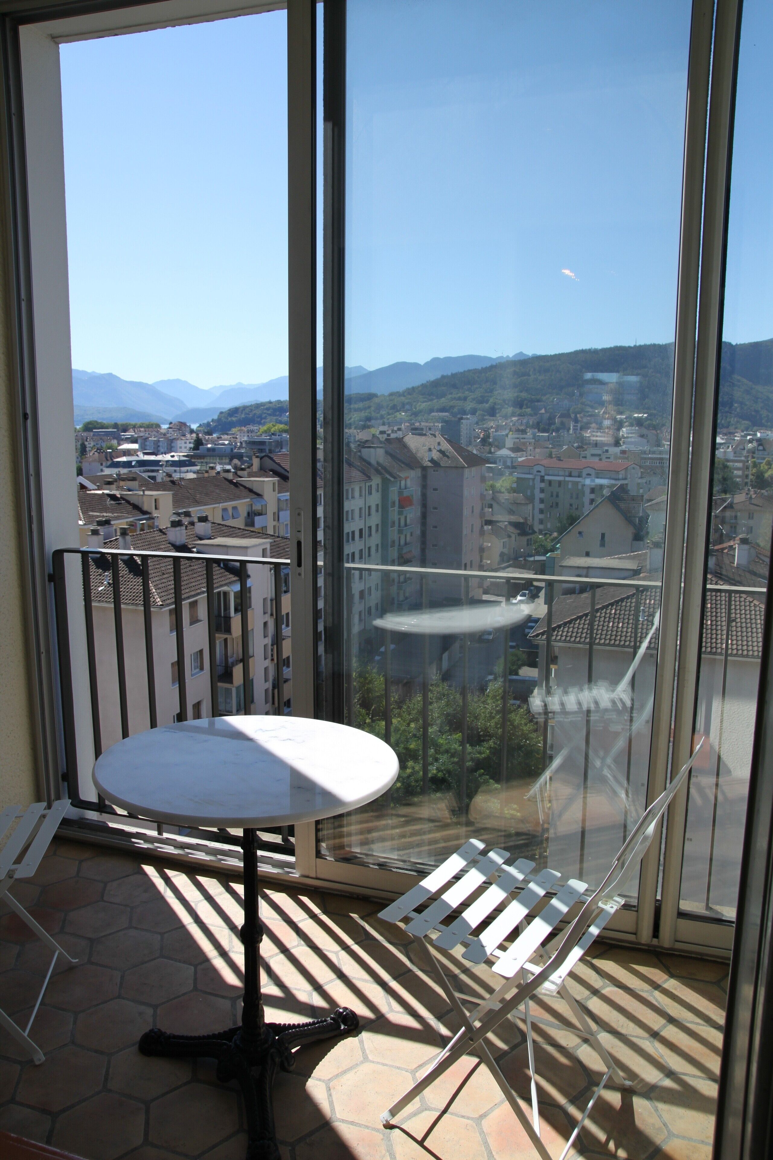 En balkon med bord og stole, der giver udsigt over by og bjerglandskab.