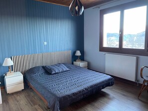 Ein Schlafzimmer mit Bett, Nachttischen, einer Lampe, einem Sessel und einem Fenster mit Blick.