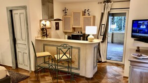 A compact living space with a kitchen area, a dining table with chairs, a television, and a door leading to an outdoor area. - CHARMING STUDIO 28m2 terrace 22m2 PANORAMA MER / MASSIF DE L'ESTEREL (Théoule-Sur-Mer)