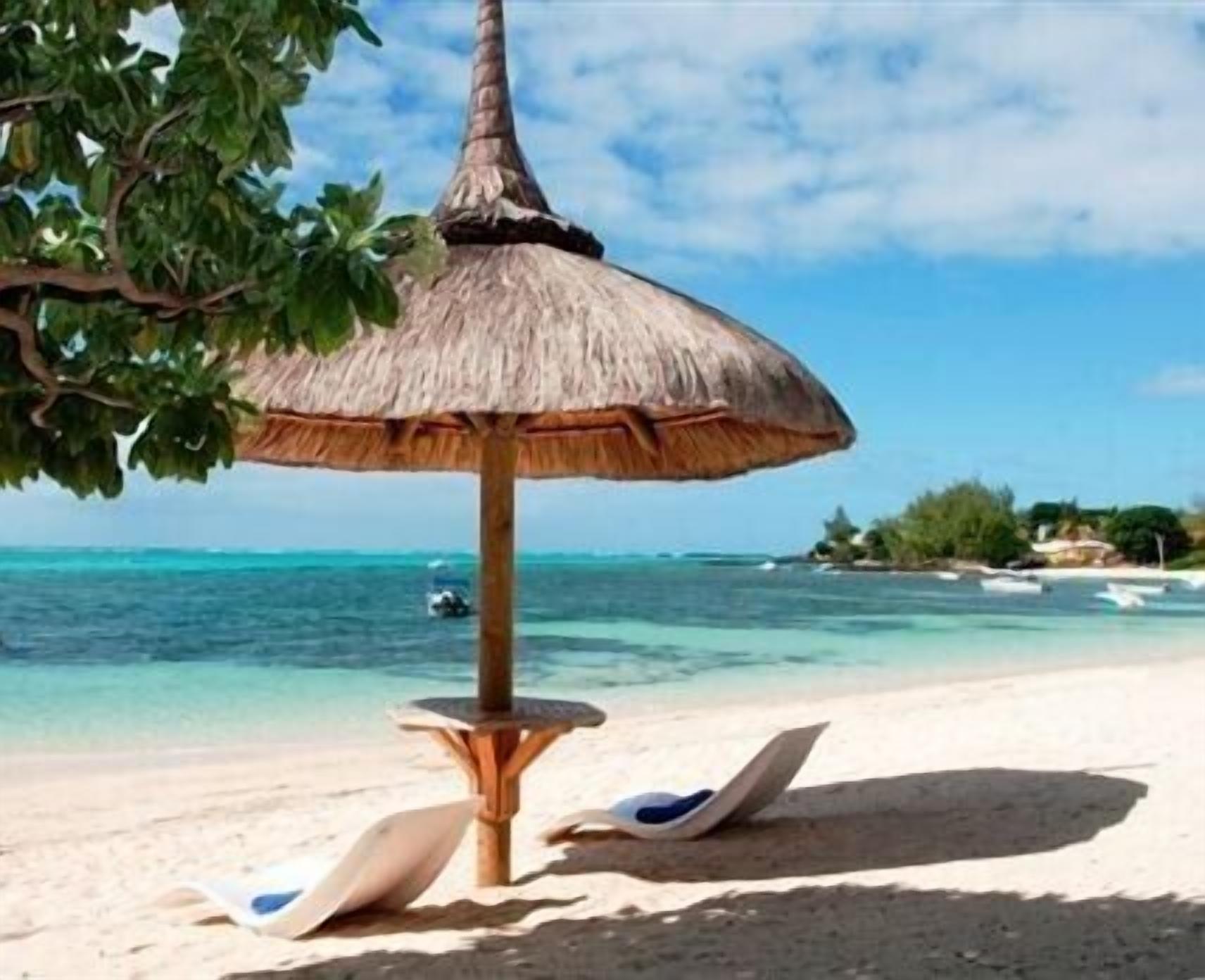 Une plage avec un parasol en chaume, une chaise longue et une vue dégagée sur l’océan.