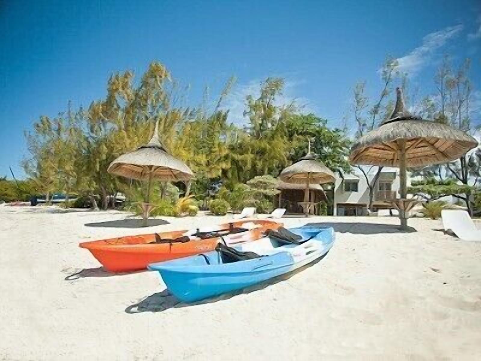 A beach with two boats, a thatched-roof structure, and a building in the background.
