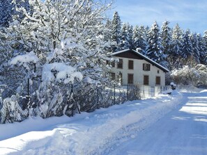 A snow-covered house with a fenced yard and a clear sky.