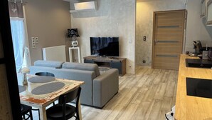 Een moderne woonkamer met een bank, televisie en een eethoek met tafel en stoelen.