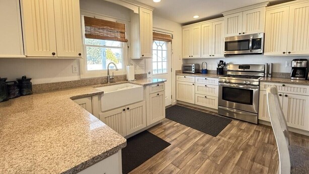 A kitchen with white cabinets, granite countertops, stainless steel appliances, and a herringbone wood floor.