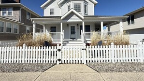 A two-story house with a front porch, a picket fence, and a clear blue sky.