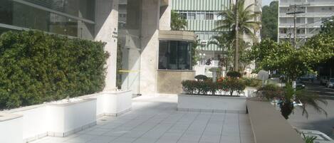 A modern building with a tiled courtyard, a glass entrance, and surrounding greenery.