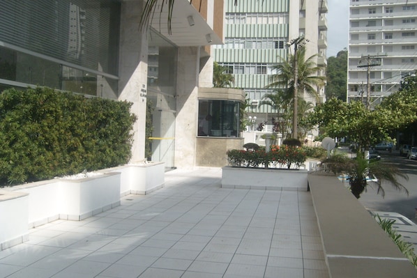 A modern building with a tiled courtyard, a glass entrance, and surrounding greenery.