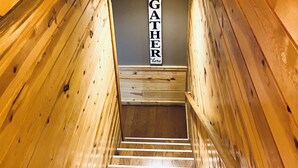 Ein Holzinnenraum mit einer Holztreppe, die zu einer unteren Ebene führt. Über der Treppe hängen zwei Holz-Eimer an der Wand, und ein Schild mit der Aufschrift 'DUCK GATHER HERE'.