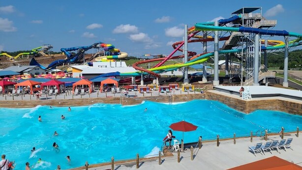 Ein Wasserpark mit einem großen Schwimmbecken, mehreren Wasserrutschen und Liegestühlen.