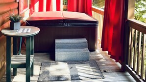 Eine Holzterrasse mit einem roten Vorhang, einem kleinen Tisch mit einer Pflanze und einer Bank.