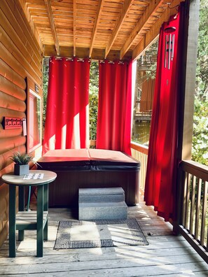 Eine Holzterrasse mit einem roten Vorhang, einem kleinen Tisch mit einer Pflanze und einer Bank.
