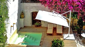Une terrasse en bois avec une piscine, des chaises longues et un parasol blanc.