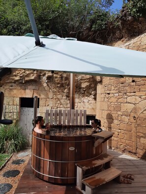 A stone-walled outdoor hot tub area with a wooden bench and a covered seating area.