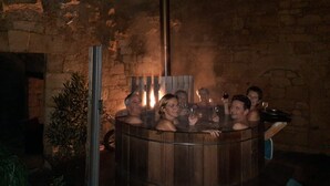 A group of people in a wooden hot tub with a stone wall background.