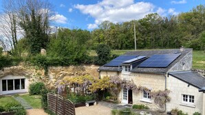 A stone house with solar panels, a gravel driveway, and a garden with plants and a wooden fence.