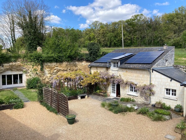 A stone house with solar panels, a gravel driveway, and a garden with plants and a wooden fence.