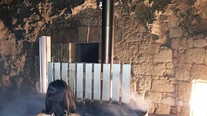 A stone-walled sauna with a wooden bench and a metal pipe emitting steam.