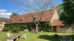 A traditional stone building with a red-tiled roof, ivy-covered walls, and a well-maintained lawn with white plastic chairs.