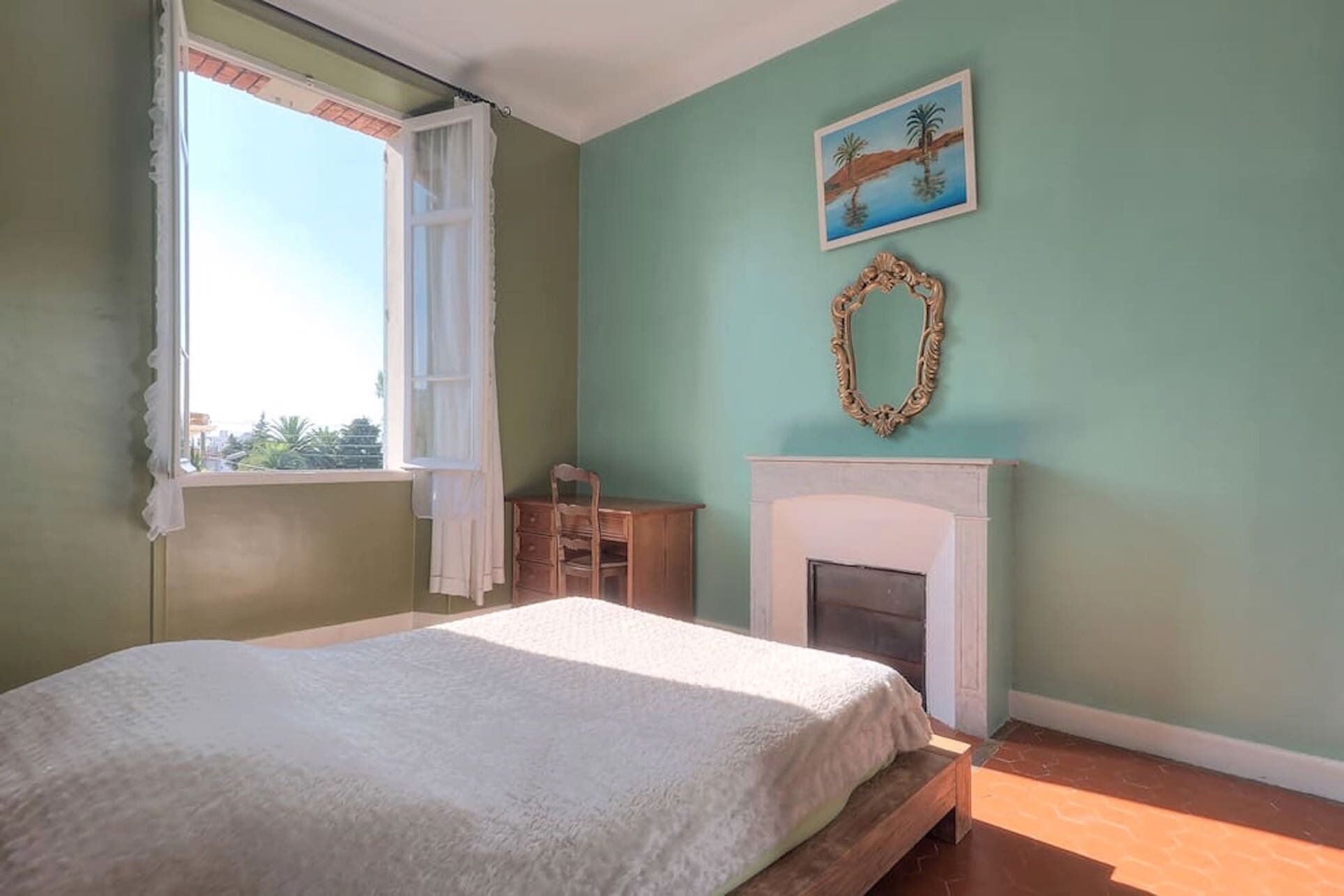 Une chambre à coucher avec un lit, une cheminée, une fenêtre avec des rideaux, une chaise et un tableau au mur.