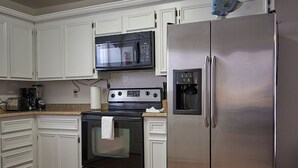 Una cocina con armarios blancos, un refrigerador de acero inoxidable, un microondas, una estufa y un dispensador de agua.