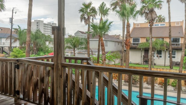 Una terraza de madera con piscina, rodeada de palmeras y edificios residenciales.